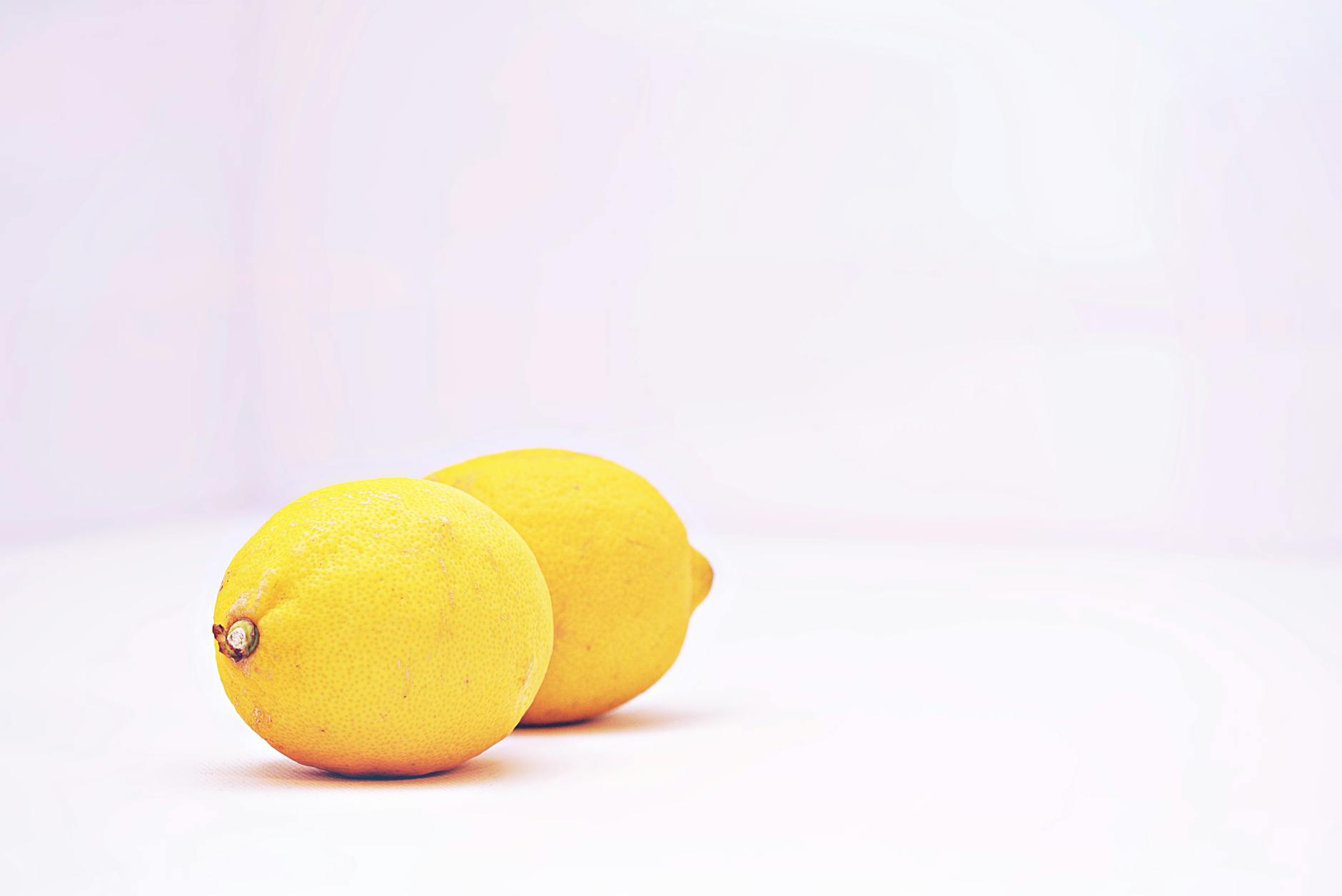 Two vibrant yellow lemons on a minimalistic white background, symbolizing freshness and calm.