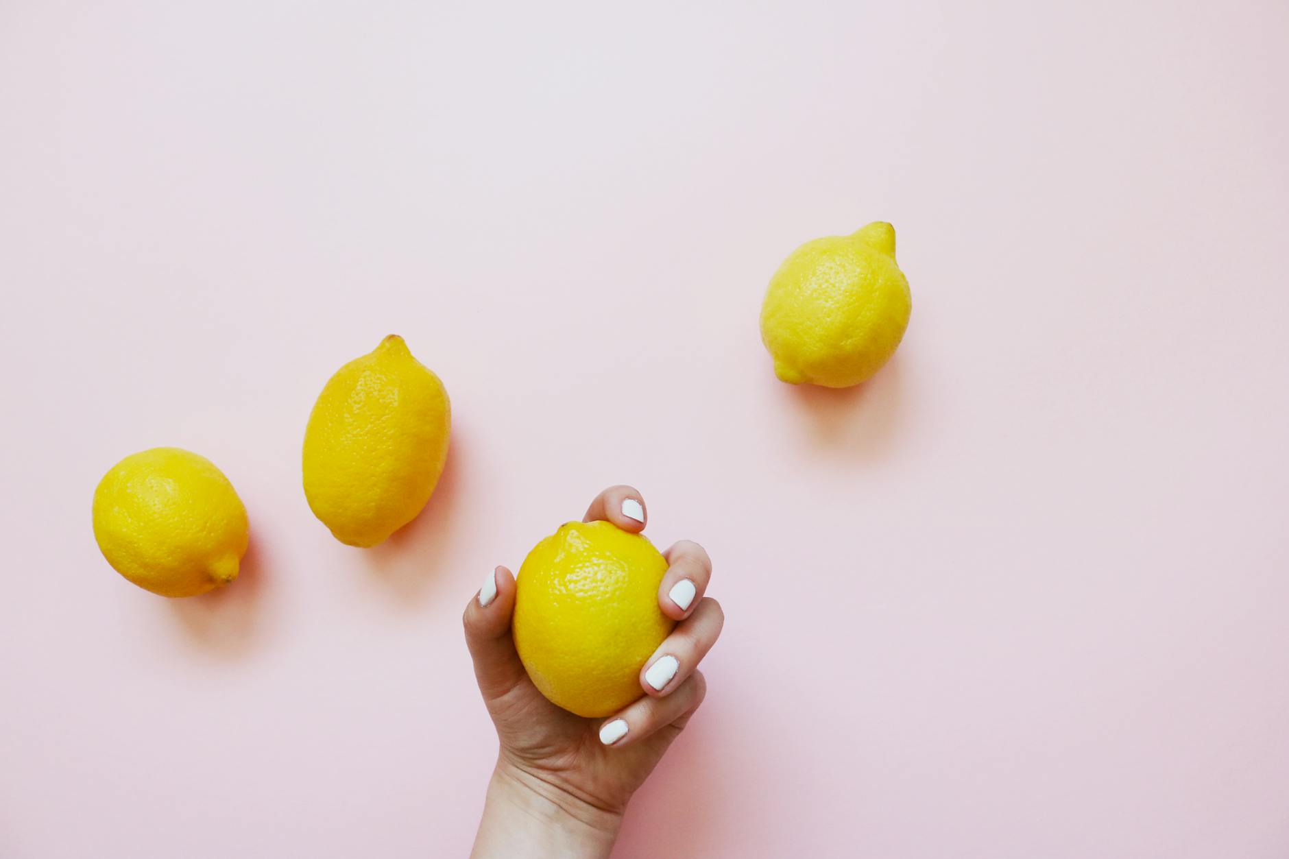 Hand holding a fresh lemon on soft pink background, symbolizing renewal and sensory reconnection