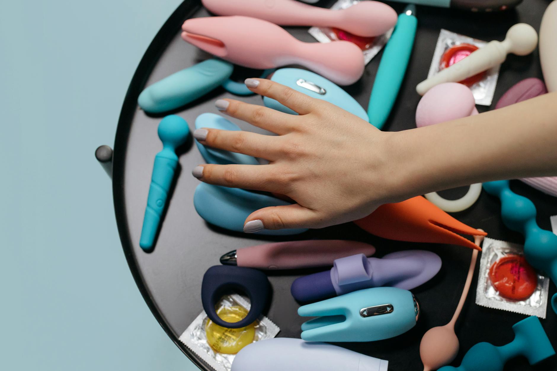 Close-up of hands holding a pink vibrator, with art books in the background