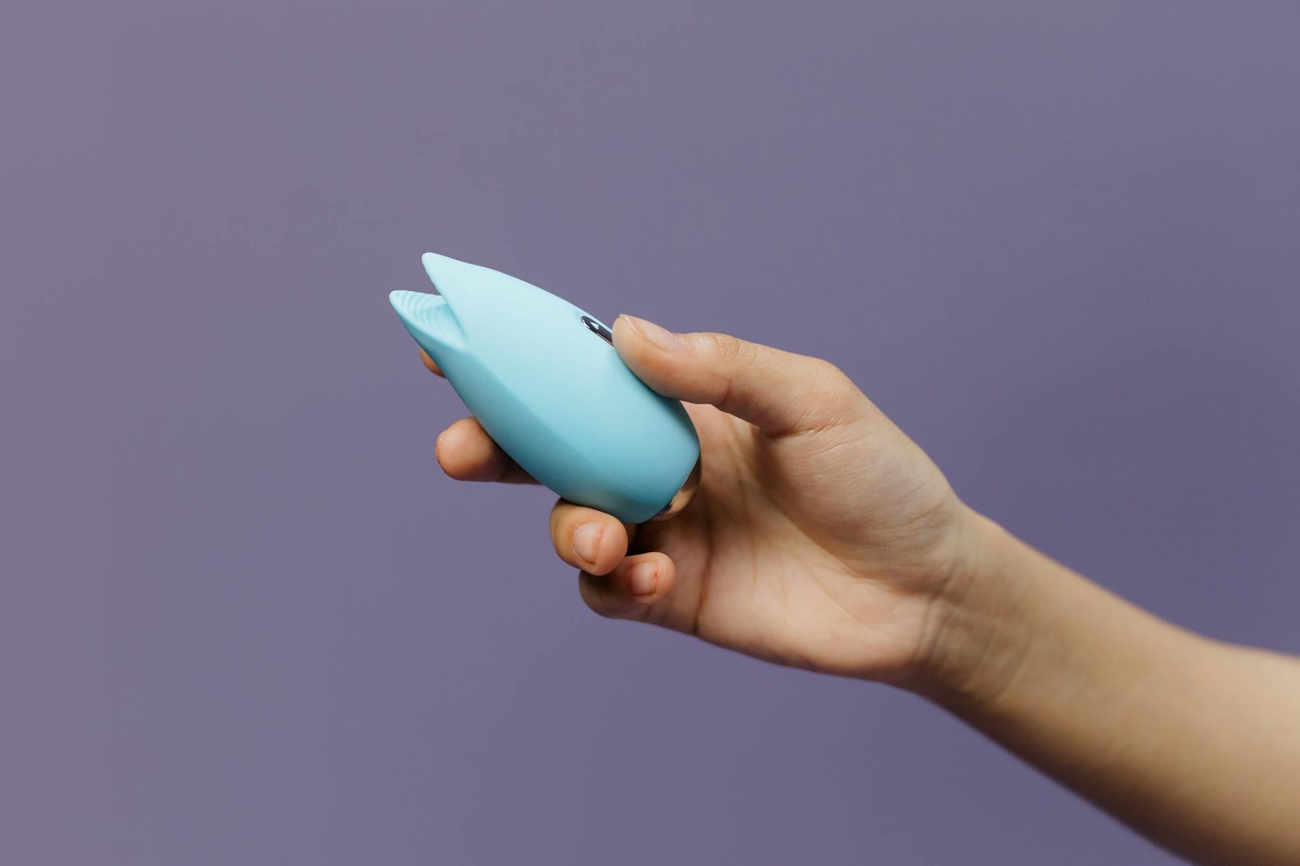 A silicone clitoral vibrator held in hand against a purple background
