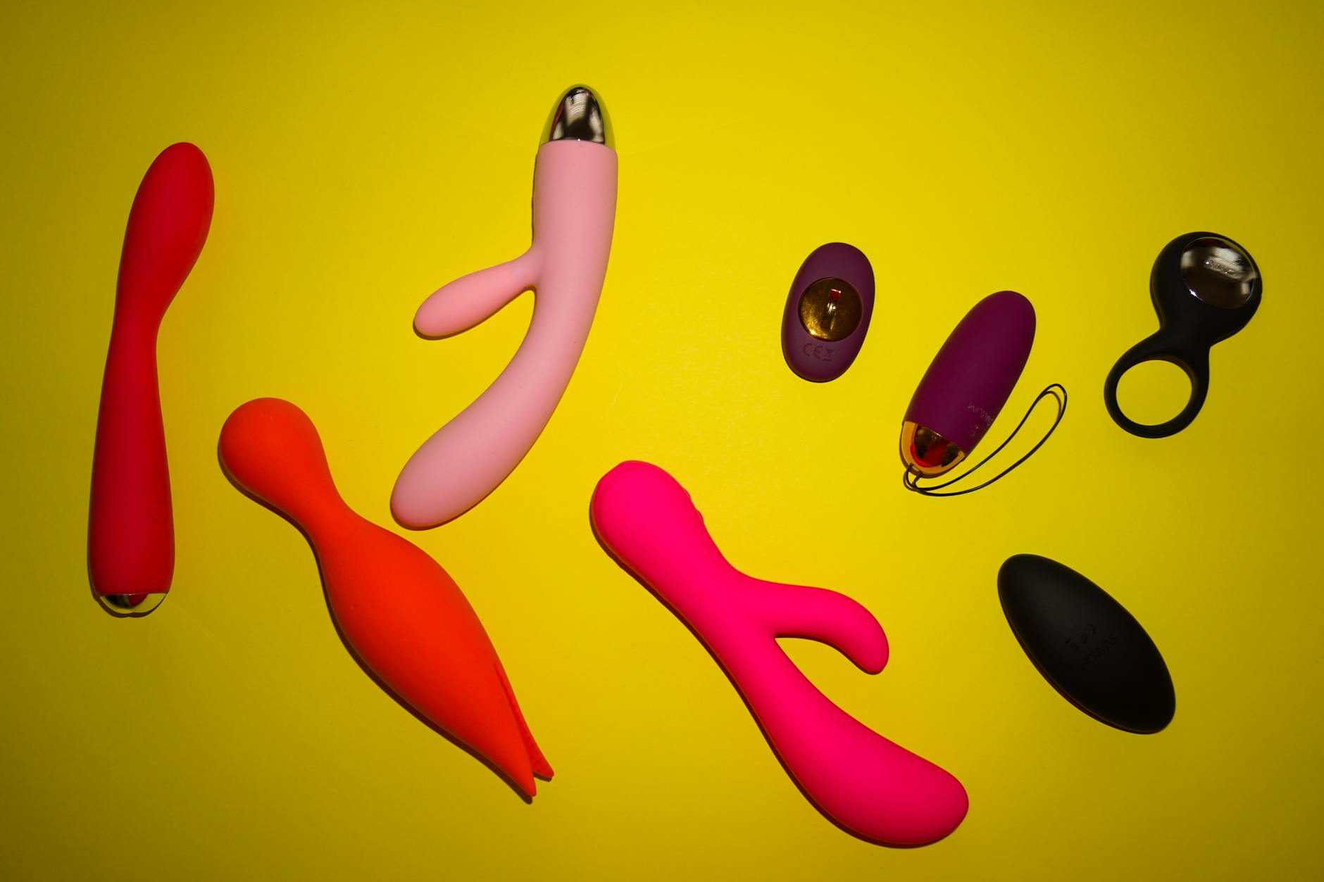 Vibrant collection of colorful clitoral vibrators and sex toys arranged on a bright yellow background