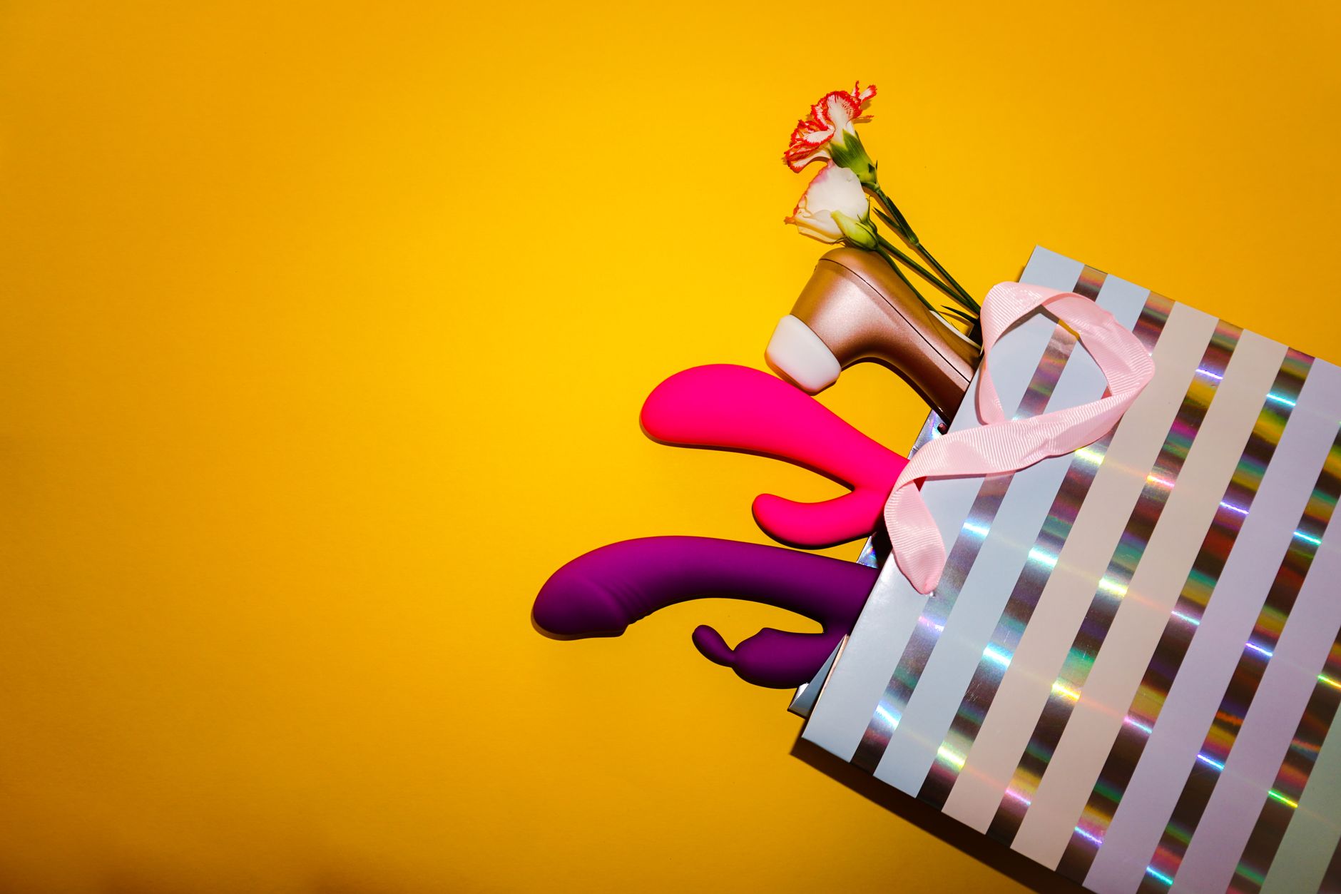 Colorful lemon vibrators and clitoral toys displayed with flowers in a holographic gift bag on a bold yellow background
