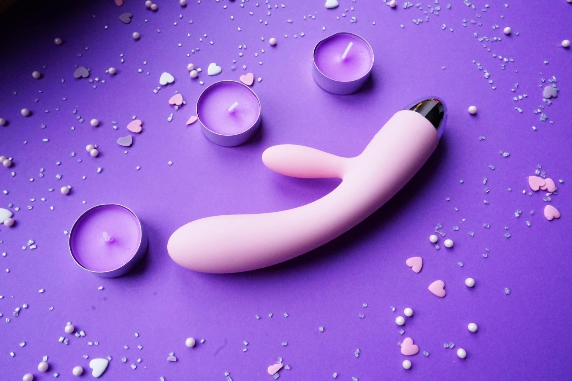 Pink lemon-shaped vibrator on purple background with heart confetti and candles